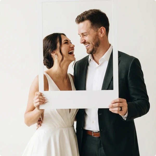 Happy bride and groom smiling while holding a white photo booth frame