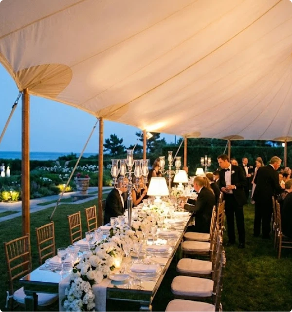 Elegant wedding dinner reception set up inside a large illuminated tent at dusk